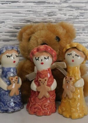 Petite figurine en faïence portant un nounours, céramique artisanale pleine de tendresse.